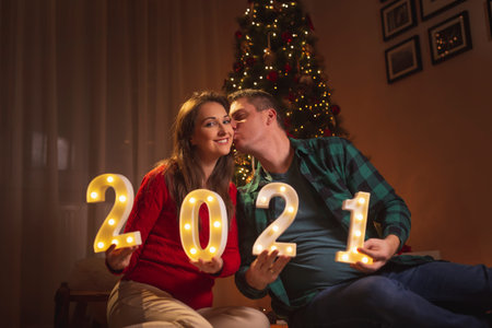 Couple in love kissing, celebrating New 2021 Year at home due to social distancing as part of Covid...