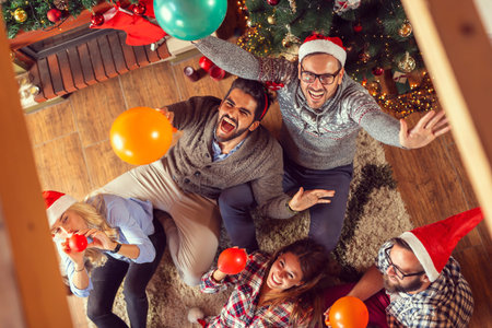 Top view of group of friends sitting next to a fireplace and Christmas tree, having fun on Christmas...