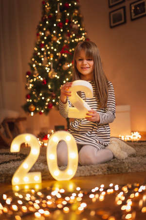 Little girl wearing costume antlers having fun while celebrating Christmas eve at home, holding a handful of Chrstmas lightsの写真素材