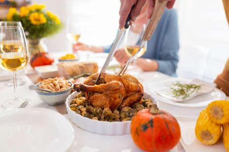 Detail of male hands cutting the chicken and the table setting for people celebrating Thanksgiving and having dinner party at homeの写真素材