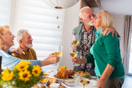 Group of senior friends having fun while celebrating Thanksgiving together at home over traditional dinner, pouring wine and making a toastの写真素材