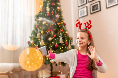 Child wearing Santa hat lying on the floor next to a nicely decorated Christmas tree, having fun at home during winter holiday seasonの写真素材