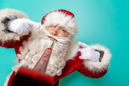 Portrait of Santa Claus holding nicely wrapped Christmas present and opening it, isolated on mint colored backgroundの写真素材