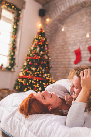 Couple in love wearing pajamas and costume reindeer antlers having fun taking selfies in bed on Christmas morningの写真素材