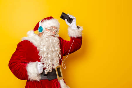 Santa Claus holding a lantern with candle and waving towards the camera isolated on yellow colored backgroundの写真素材
