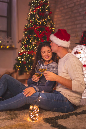 Young couple in love sitting by nicely decorated Christmas tree, enjoying beauty of winter holiday season, holding a jar filled with Christmas lights and relaxing at homeの写真素材