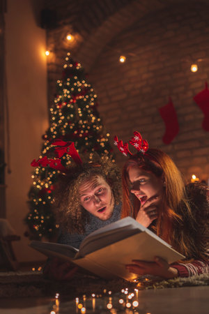 Couple in love sitting by the Christmas tree, drinking wine, celebrating New Year at home with  illuminated numbers 2021 representing the upcoming New Year in the foregroundの写真素材