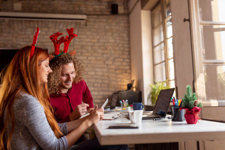 Young business people wearing costume reindeer antlers while working in an office around Christmas, bringing winter holiday spirit into workplaceの写真素材