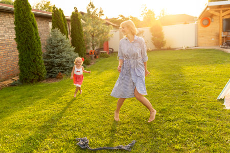 Mother and daughter having fun playing in the backyard on a sunny summer day, running, chasing and trying to catch each otherの写真素材