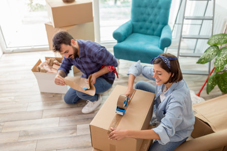 Beautiful young couple in love having fun unpacking things from cardboard boxes while moving in...