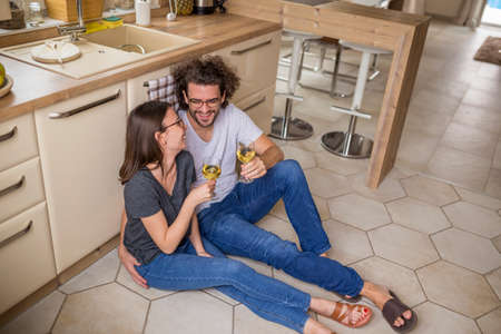 Beautiful young couple in love doing the washing up together after lunch; woman washing the dishes while man is wiping them using kitchen clothの写真素材