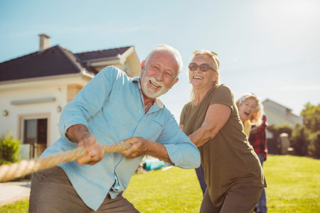 Senior people having fun playing tug of war, spending sunny summer day outdoors; group of elderly...