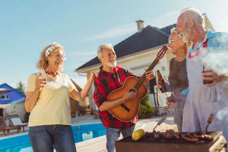 Senior neighbors having fun spending sunny summer day together outdoors, grilling meat and relaxingの写真素材