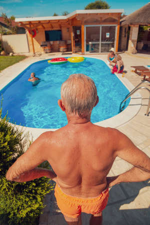 Group of senior people having fun spending hot sunny summer day at the swimming pool, playing with water guns, splashing water on each otherの写真素材