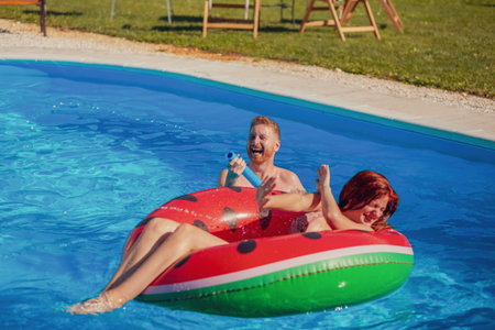 Beautiful young couple in love having fun swimming and splashing water on each other in the pool,...