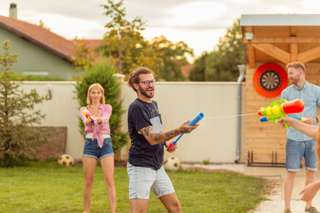 Group of young friends having fun spending summer day outdoors, playing with squirt guns, splashing...