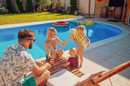 Cheerful parents having fun playing with their children with squirt guns by the swimming pool splashing water on each other, enjoying summer vacationの写真素材
