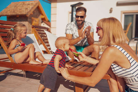 Cheerful parents having fun playing with their children with squirt guns by the swimming pool splashing water on each other, enjoying summer vacationの写真素材