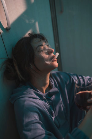 Upset woman sitting on the floor in the dark, holding a gun and crying after committing murder in...
