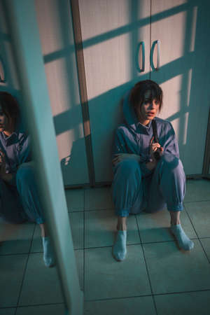 Upset woman sitting on the floor in the dark, holding a gun and crying after committing murder in self-defense; scared woman victim of domestic violence holding a gun for self-defenseの写真素材