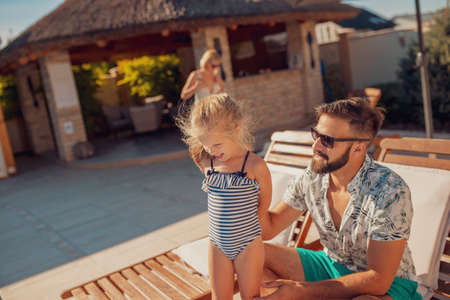 High angle view of young parents having fun playing with their daughter in the swimming pool, enjoying hot sunny summer day outdoors and relaxing while on a vacationの写真素材