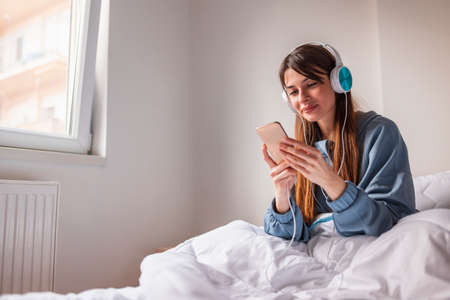 Beautiful pensive young woman wearing pajamas sitting in bed in the morning, reading a book and relaxing at homeの写真素材