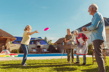 Group of cheerful active senior people having a backyard barbecue party, grilling meat and vegetables and having fun playing badmintonの写真素材
