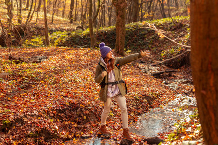 Beautiful young active woman crossing the creek while hiking on a sunny autumn day in forest,...