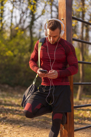Athletic young man carrying gym bag, drinking water after an intense outdoor workout in a street...