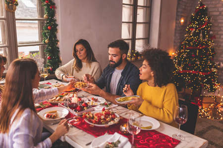 High angle view of group of friends making a toast during Christmas dinner, raising glasses of wine and celebrating Christmas day together at homeの写真素材