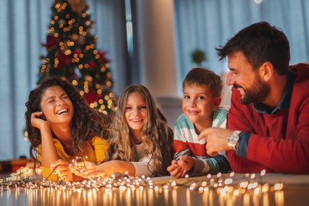 Parents celebrating New Years Eve at home with kids, sitting by the Christmas tree, holding...