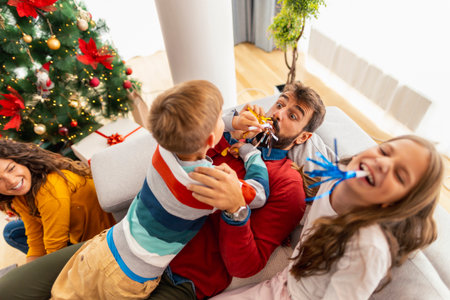 Parents having fun playing with children while spending Christmas at home, blowing party whistles and laughingの写真素材