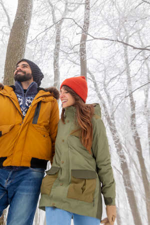 Beautiful young couple in love enjoying snowy winter day outdoors, taking a walk through a forestの写真素材