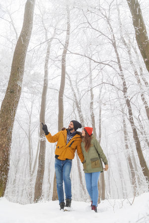 Beautiful young couple in love enjoying snowy winter day outdoors, taking a walk through a forest