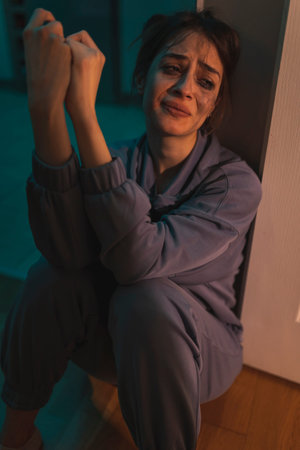 Depressed drunk woman sitting on the floor in the dark with smeared makeup, drinking wine from a...