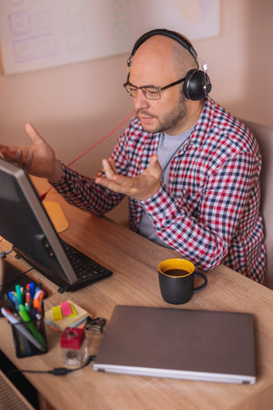 Freelancer sitting at his desk, holding smart phone and taking notes in planner while working in...
