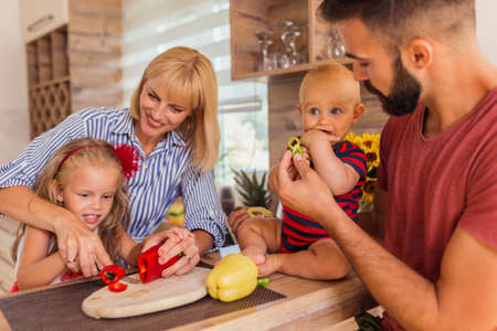 Beautiful happy parents and children having fun preparing food and cutting vegetables for lunch, enjoying leisure time together at homeの写真素材