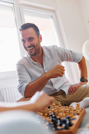 Couple in love sitting on couch in living room, having fun playing chess and enjoying leisure time at homeの写真素材