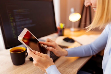 Woman sitting at her desk in home office, typing text message using smart phone while workingの写真素材
