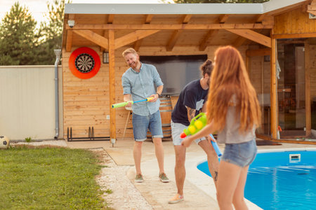 Group of young friends having fun spending summer day outdoors, playing with squirt guns, splashing...