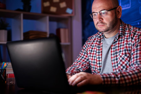 Man sitting at his desk, using laptop computer while working late in home office