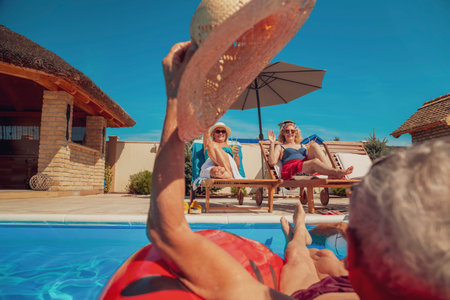 Group of elderly people having fun spending hot summer day at the swimming pool, sunbathing,...