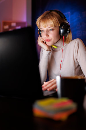 Woman sitting at her desk stretching out while working overtime in home office late at nightの写真素材