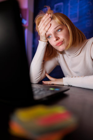 Woman working overtime in home office late at night, yawning while sitting at her desk