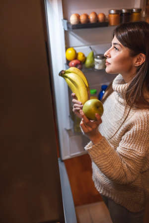 Beautiful young woman wearing pajamas having fun playing video games in bed at nightの写真素材