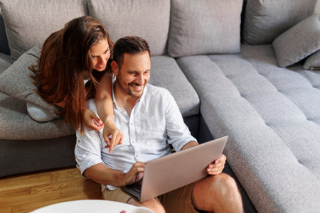 Couple in love enjoying leisure time at home, drinking take away coffee and surfing the Internet using laptop computer and smart phoneの写真素材
