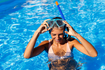 Attractive young woman leaning on the edge of a swimming pool, relaxing while on summer vacation,...
