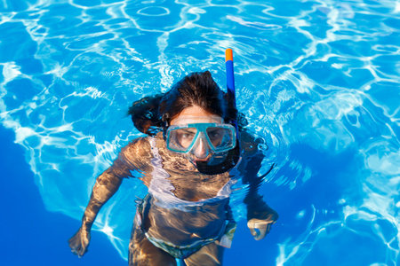 Attractive young woman leaning on the edge of a swimming pool, relaxing while on summer vacation,...