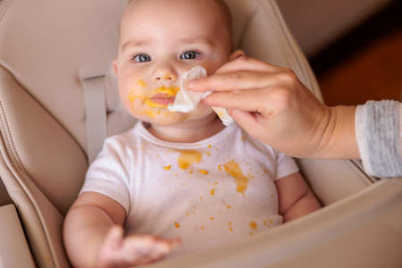 High angle view of mother feeding cheerful baby boy with porridge using spoon, baby sitting in high chair all messy and staied smiling and eatingの写真素材