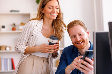 Colleagues working together on a new project in modern office, drinking coffee and using smart phone and desktop computersの写真素材